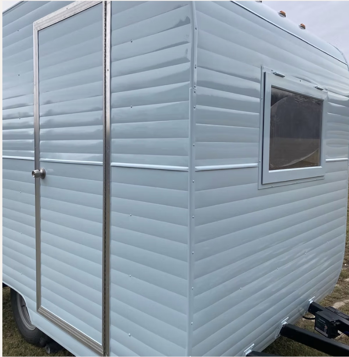 Close-up of a restored trailer clad in pale blue ribbed aluminum siding with polished trim